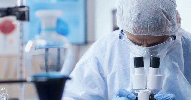 Chemist researcher doctor wearing ppe equipment to prevent infection with coronavirus analyzing virus sample using microscope working at medical vaccine in chemistry laboratory. Medicine concept